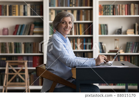 Mature businesswoman sit at desk with laptop staring at camera 88015170