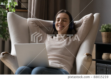 Woman relaxing on armchair with laptop, enjoy music through headphones Woman relaxing on armchair with laptop, enjoy music through headphones 88015219