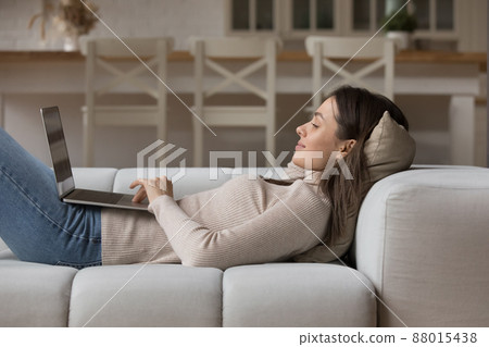 Relaxed young woman lying on cozy sofa with laptop 88015438