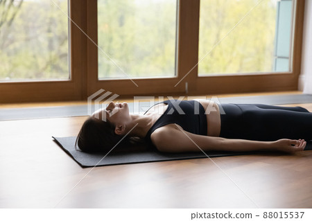 Woman lying on mat doing Corpse or Dead Body asana 88015537