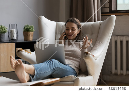 Woman put computer on laps talking on smartphone Woman put computer on laps talking on smartphone 88015668