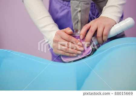 A female client receives a LPG massage in a beauty clinic. Beauty parlour. Blue suit. Lilac background. 88015669