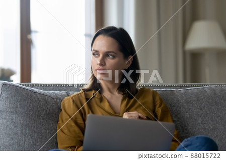 Woman sit on couch with laptop staring aside looking pensive 88015722
