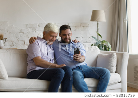 Grownup son his older father having fun using modern smartphone Grownup son his older father having fun using modern smartphone 88015759