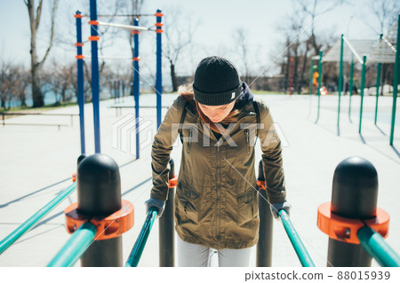 Young woman in casual warm clothes doing parallel bars exercises Young woman in casual warm clothes doing parallel bars exercises 88015939