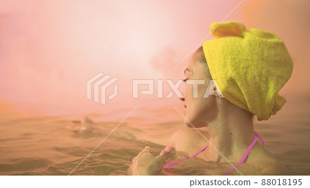 Close up caucasian woman in a swim in hot saline mineral water bath at a traditional spa outdoor with soft magic pink lighting steam. Geothermal spa. 88018195