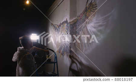 Artist designer draws an eagle on the wall. Craftsman decorator paints picture with acrylic oil color. Painter painter dressed in paint coat. Indoor. Artist designer draws an eagle on the wall. Craftsman decorator paints picture with acrylic oil color. Painter painter dressed in paint coat. Indoor. 88018197