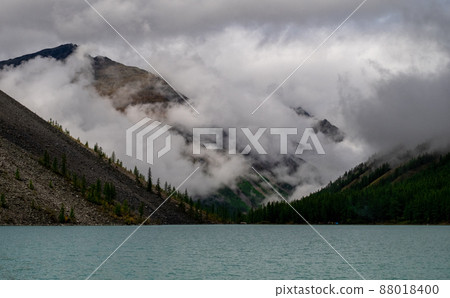 Shavlinskoye lake in the Altai Republic on the background of mountain peaks shrouded in fog. Shavlinskoye lake in the Altai Republic on the background of mountain peaks shrouded in fog. 88018400