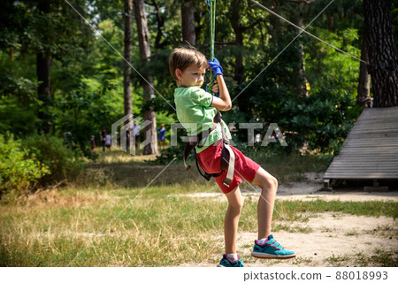 Strong excited young boy playing outdoors in rope park. Caucasian child dressed in casual clothes and sneakers at warm sunny day. Active leisure time with children concept 88018993