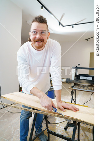 carpenter in protective gloves and glasses cuts bark from wood with chisel carpenter in protective gloves and glasses cuts bark from wood with chisel 88019257