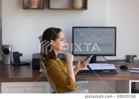 Pensive woman holds smartphone sit at workplace desk with computer 88020198