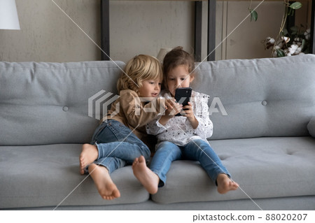 Happy little adorable kids playing games on cellphone. Happy little adorable kids playing games on cellphone. 88020207