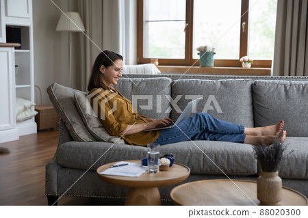 Side view woman sits on sofa texting message using laptop Side view woman sits on sofa texting message using laptop 88020300