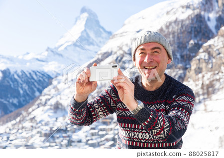 Cheerful traveler filming on phone his hike in Swiss Alps on winter day 88025817