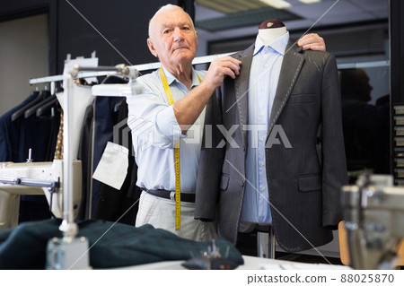 Experienced tailor threading jacket before starting work in workshop 88025870