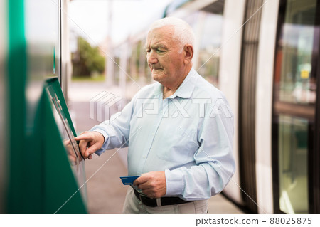 Senior man using ATM machine while standing on tram station 88025875