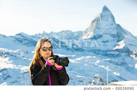 Woman photographer in sunglasses capturing mountain views in winter 88026098