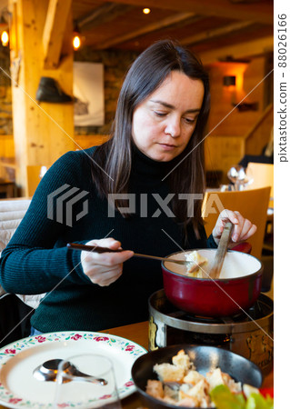 Young adult woman eating fondue at restaurant 88026166