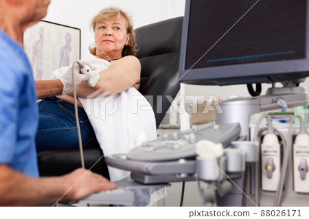 Elderly man sonographer using ultrasonography machine checking female patient in hospital diagnostic room 88026171