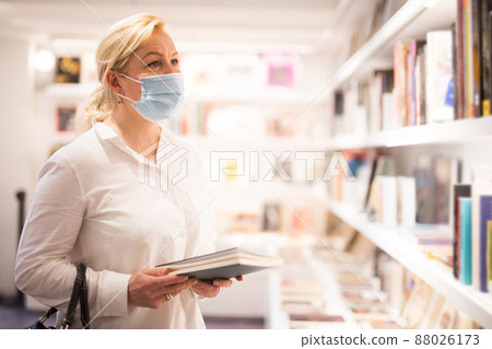 Mature woman in face mask looking at souvenir products Mature woman in face mask looking at souvenir products 88026173