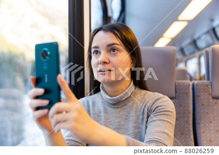 Woman enjoying journey in train, taking pictures on cellphone Woman enjoying journey in train, taking pictures on cellphone 88026259