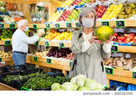Woman in mask choosing melon in greengrocer Woman in mask choosing melon in greengrocer 88026260