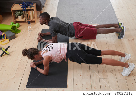 Horizontal high angle view shot of modern ethnically diverse couple spending time at home doing plank exercise Horizontal high angle view shot of modern ethnically diverse couple spending time at home doing plank exercise 88027112