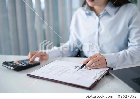 Portrait of  Asian Business woman working from office taking reading and writing notes in note pad working on laptop computer  in her workstation 88027352