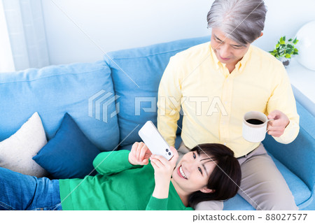 Parent and child of middle father and young daughter relaxing on the sofa in the living room Parent and child of middle father and young daughter relaxing on the sofa in the living room 88027577