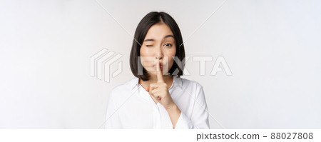 Close up portrait of young asian woman making hush, shhh shush sign, press finger to lips, dont speak, keep quiet gesture, white background 88027808