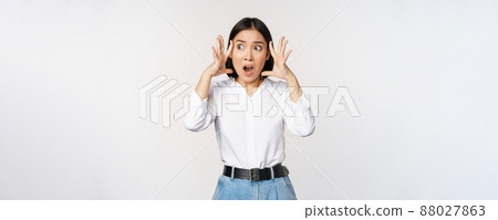 Image of shocked anxious asian woman in panic, holding hands on head and worrying, standing frustrated and scared against white background 88027863