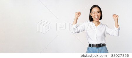 Enthusiastic asian woman rejoicing, say yes, looking happy and celebrating victory, champion dance, fist pump gesture, standing over white background Enthusiastic asian woman rejoicing, say yes, looking happy and celebrating victory, champion dance, fist pump gesture, standing over white background 88027866