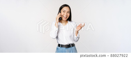 Friendly smiling asian woman talking on phone, girl on call, holding smartphone and laughing, speaking, standing over white background 88027922