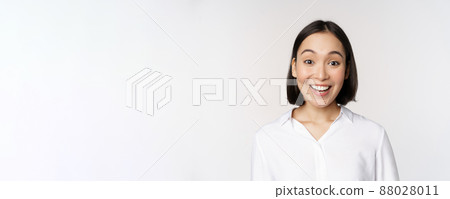 Close up portrait of young asian female model looking amazed at camera, smiling white teeth, standing against white background Close up portrait of young asian female model looking amazed at camera, smiling white teeth, standing against white background 88028011