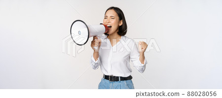 Enthusiastic asian woman, girl activist shouting at protest, using megaphone, looking confident, talking in loudspeaker, protesting, standing over white background 88028056