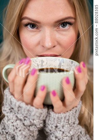 An attractive blonde woman covers her face with a large cup of coffee. 88028385