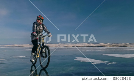 Woman is riding bicycle on the ice. Tires on bike are covered wi Woman is riding bicycle on the ice. Tires on bike are covered wi 88028438