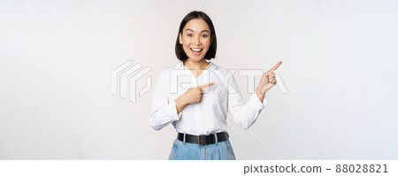Portrait of beautiful asian woman, saleswoman pointing fingers right and showing info, banner or logo, sale advertisement, standing over white background Portrait of beautiful asian woman, saleswoman pointing fingers right and showing info, banner or logo, sale advertisement, standing over white background 88028821