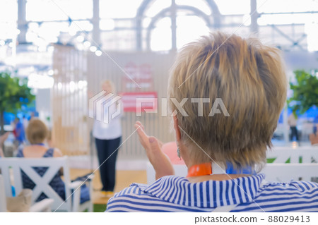 Woman listening to speech of unrecognizable lecturer at conference - back view Woman listening to speech of unrecognizable lecturer at conference - back view 88029413