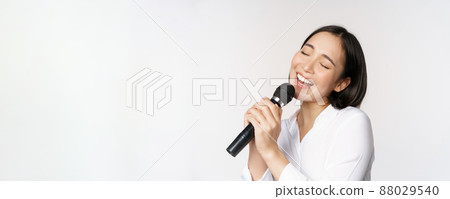 Close up portrait of asian woman singing in microphone at karaoke, standing over white background Close up portrait of asian woman singing in microphone at karaoke, standing over white background 88029540