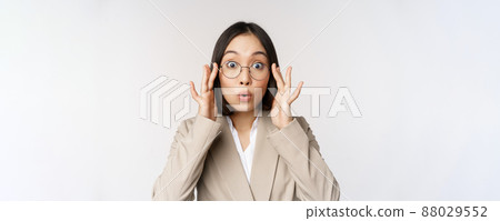 Portrait of asian businesswoman in glasses, looking surprised amazed at camera, standing in suit over white background Portrait of asian businesswoman in glasses, looking surprised amazed at camera, standing in suit over white background 88029552