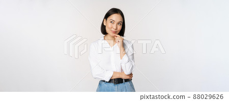 Image of thoughtful smiling woman has an idea, scheming, planning, looking aside and thinking, standing in office white blouse against studio background Image of thoughtful smiling woman has an idea, scheming, planning, looking aside and thinking, standing in office white blouse against studio background 88029626