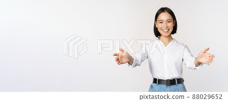 Image of smiling asian woman welcoming guests clients, businesswoman stretching out open hands, greeting, standing over white background Image of smiling asian woman welcoming guests clients, businesswoman stretching out open hands, greeting, standing over white background 88029652