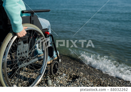 Caucasian woman in a wheelchair on the seashore. Close-up of female hands. Caucasian woman in a wheelchair on the seashore. Close-up of female hands. 88032262