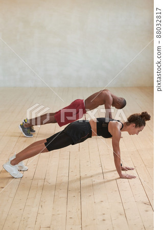 Vertical studio shot of sporty young Black man and Caucasian woman doing strengthening plank exercise in loft studio room 88032817