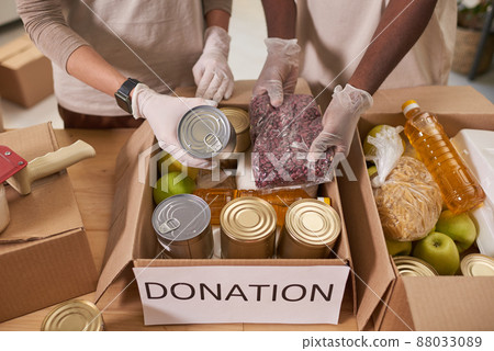 High angle shot of unrecognizable man and woman wearing protective gloves packing food supplies into cardboard boxes for charity High angle shot of unrecognizable man and woman wearing protective gloves packing food supplies into cardboard boxes for charity 88033089