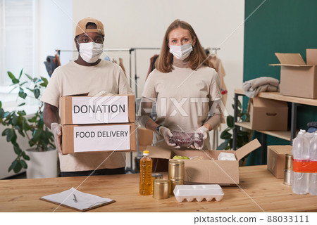 Medium portrait of young adult man and woman wearing protective masks and gloves working together in charity looking at camera 88033111