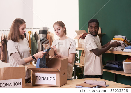 Group of three modern young volunteers working together in charity organization sorting out clothes 88033208