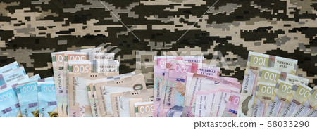 Ukrainian hryvnya bills on fabric with texture of Ukrainian military pixeled camouflage. Cloth with camo pattern in grey, brown and green pixel shapes 88033290