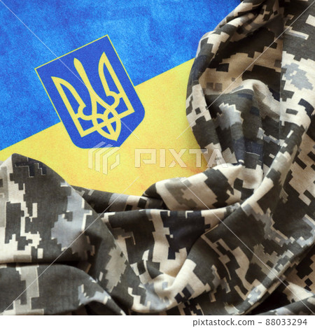 Ukrainian flag and coat of arms with fabric with texture of pixeled camouflage. Cloth with camo pattern in grey, brown and green pixel shapes with Ukrainian trident sign Ukrainian flag and coat of arms with fabric with texture of pixeled camouflage. Cloth with camo pattern in grey, brown and green pixel shapes with Ukrainian trident sign 88033294